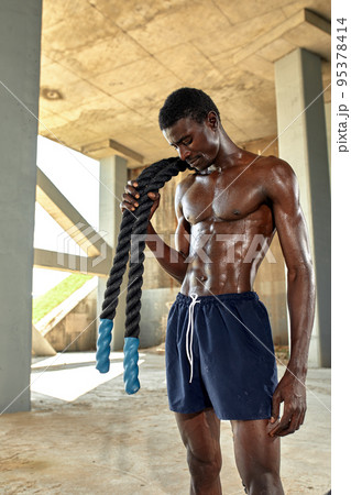 Rope workout. Sport man doing battle ropes exercise outdoor. Black male athlete exercising, doing functional fitness training with heavy rope Rope workout. Sport man doing battle ropes exercise outdoor. Black male athlete exercising, doing functional fitness training with heavy rope 95378414