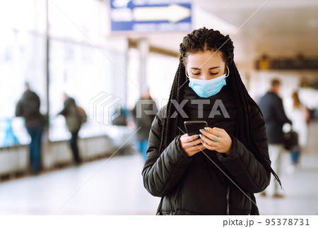 Girl in protective sterile mask on her face with a phone in quarantine city. Woman using the phone. 95378731