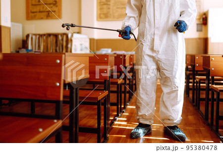 Man wearing protective suit disinfecting school class with spray chemicals to preventing the spread. Man wearing protective suit disinfecting school class with spray chemicals to preventing the spread. 95380478