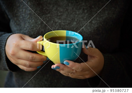 A mug in the colors of the Ukrainian flag in hands. A mug in the colors of the Ukrainian flag in hands. 95380727
