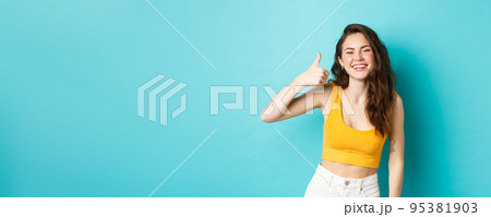 Summer holidays and emotions concept. Cheerful beauty girl with curly hairstyle and cropped top, showing yes thumb up gesture and laughing, standing over blue background Summer holidays and emotions concept. Cheerful beauty girl with curly hairstyle and cropped top, showing yes thumb up gesture and laughing, standing over blue background 95381903