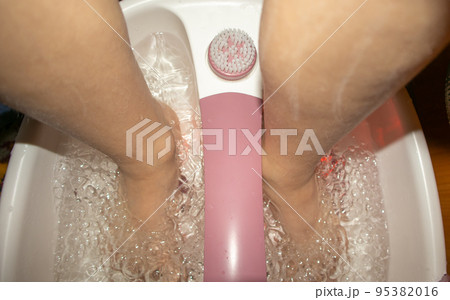Close-up of feet in a tub with a vibrating foot massager. Electric foot massage bath and water bubbles. Pedicure and foot care Close-up of feet in a tub with a vibrating foot massager. Electric foot massage bath and water bubbles. Pedicure and foot care 95382016