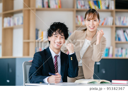 塾で受験勉強する男子高校生と女性講師 95382367