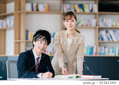 塾で受験勉強する男子高校生と女性講師 95382369