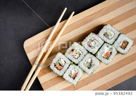 Uramaki sushi roll on wooden bamboo tray on black background. Uramaki sushi roll on wooden bamboo tray on black background. 95382492