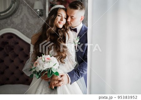 Beautiful young wedding couple posing with bouquet of flowers in hands Beautiful young wedding couple posing with bouquet of flowers in hands 95383952