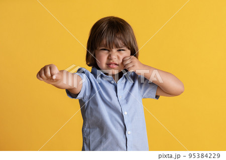 Kids anger and emotions. Furious little boy showing fists to camera, feeling annoyed, orange studio background Kids anger and emotions. Furious little boy showing fists to camera, feeling annoyed, orange studio background 95384229