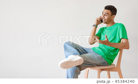 Ideas for business, modern work and communication. Young arab man talking on cellphone, sitting on chair over light wall Ideas for business, modern work and communication. Young arab man talking on cellphone, sitting on chair over light wall 95384240