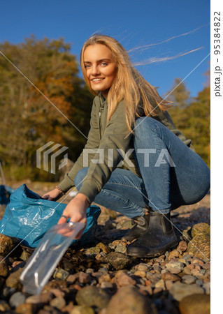 Smiling young woman in environment conservation team picking up plastic at beach Smiling young woman in environment conservation team picking up plastic at beach 95384822