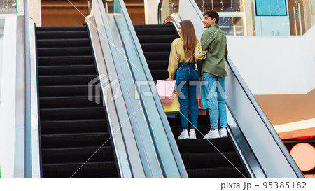 Buyers Couple Standing On Moving Stairs In Mall, Back View 95385182