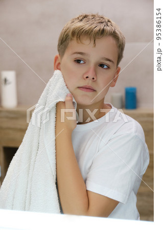 Reflection of schoolboy wiping his face with a towel after washing in bathroom. Reflection of schoolboy wiping his face with a towel after washing in bathroom. 95386154