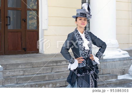 a woman dressed as a 19th century noblewoman stands near an old manor house.russian winter 95386303