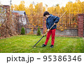 Little boy with a rake cleaning fallen leaves in the autumn yard garden. Kids and housework concept. Little boy helping with backyard cleaning. Children play outdoors. Little helper. 95386346