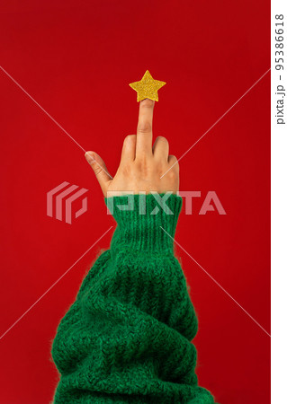 Hand in green sweater, middle finger with star raised up, abstract symbol of Christmas tree Hand in green sweater, middle finger with star raised up, abstract symbol of Christmas tree 95386618