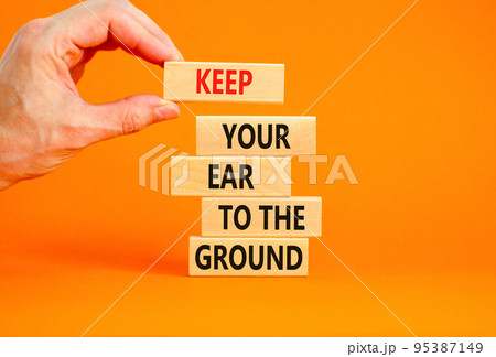 Keep your ear to the ground symbol. Concept words Keep your ear on the ground on wooden blocks. Businessman hand. Beautiful orange background. Business keep your ear on the ground concept. Copy space. 95387149