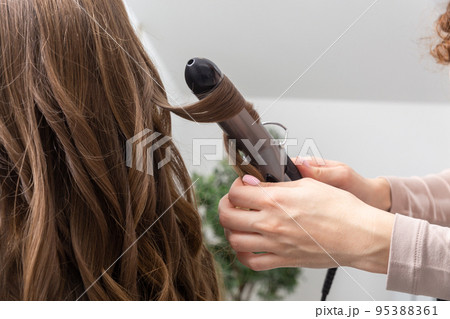 Hair stylist prepares woman makes curls hairstyle with curling iron. Hair stylist prepares woman makes curls hairstyle with curling iron. 95388361