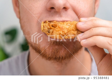 A man bites and chews a fried chicken wing in 95388481