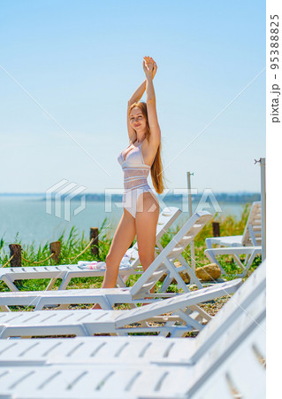 a long-haired, slender, beautiful woman in a swimsuit by a chaise longue by sea. a long-haired, slender, beautiful woman in a swimsuit by a chaise longue by sea. 95388825