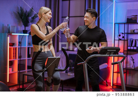 Blond caucasian sports women in sportswear cycling bike and fit asian man running on treadmill 95388863