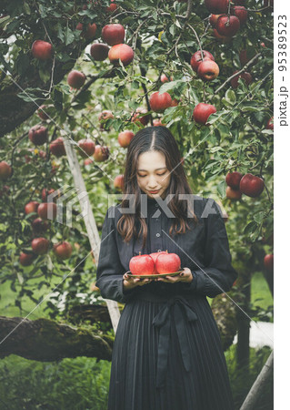 果樹園のなかで黒いワンピースを着てリンゴを持っている女性 95389523