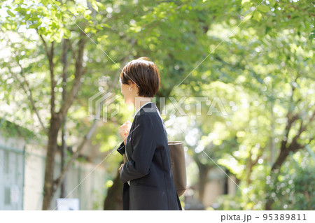 緑の中を歩くスーツの女性 95389811