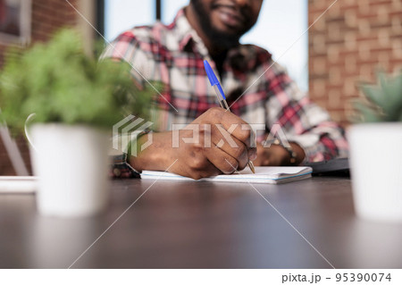 Business student taking notes on papers, doing remote job on notebook and textbook with computer. Writing report information and working on startup paperwork or documents. Close up. Business student taking notes on papers, doing remote job on notebook and textbook with computer. Writing report information and working on startup paperwork or documents. Close up. 95390074