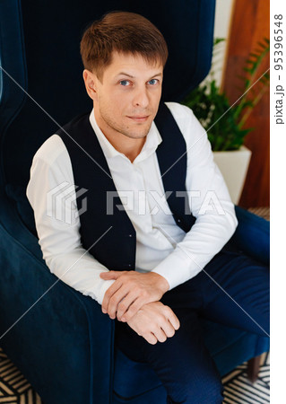 a man with a white shirt and a suit vest sits in a chair. a man with a white shirt and a suit vest sits in a chair. 95396548