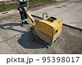 Worker use vibratory plate compactor at road construction site 95398017