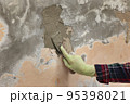 Worker spreading plaster to damaged wall 95398021