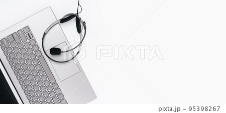 Top view of slim laptop with headset on white desk. Monochrome background. Distant learning. working from home, online courses or support. Audio podcast headphones . Helpdesk or call center banner 95398267