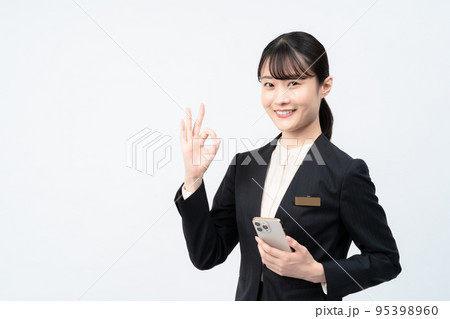 スマホを持つスーツの女性（白バック、OKポーズ） 95398960