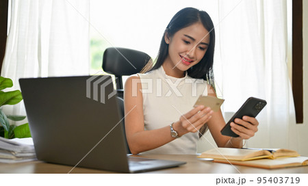 Gorgeous Asian businesswoman register her credit card number on a mobile banking app. Gorgeous Asian businesswoman register her credit card number on a mobile banking app. 95403719