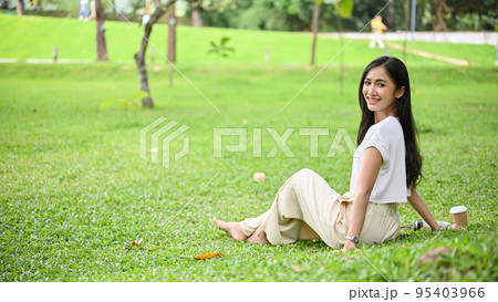 Attractive Asian female sitting on green grass in beautiful and amazing park or garden. 95403966
