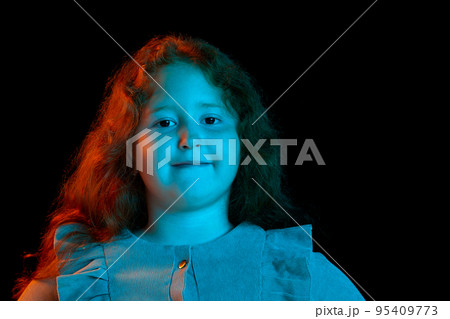 Charming redheaded little girl wearing festive dress looking at camera isolated over dark background in neon light. Kids emotions, facial expressions, fashion Charming redheaded little girl wearing festive dress looking at camera isolated over dark background in neon light. Kids emotions, facial expressions, fashion 95409773