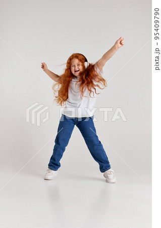 Joyful little girl, kid in white t-shirt and jeans listening to music and dancing isolated over white background. Kids fashion, emotions, carefree childhood 95409790