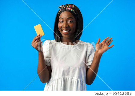Young african woman holding credit card in hand against blue background 95412685