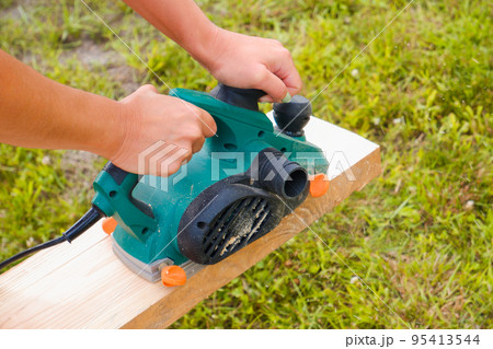 The woman planes the board. Close-up on hands with an electric plane. Working with a power tool. 95413544