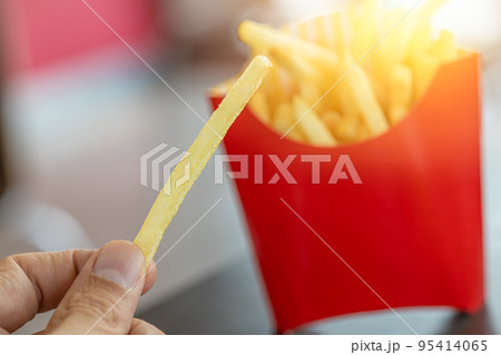 french fries. closeup male hand holding golden potato stick fry popular american fast food. 95414065