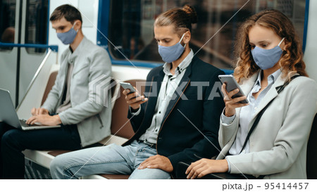 young people in protective masks sitting at a safe distance in the subway car. 95414457
