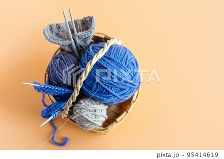 Blue balls of knitting threads on a orange background in a basket with knitting needles Blue balls of knitting threads on a orange background in a basket with knitting needles 95414619