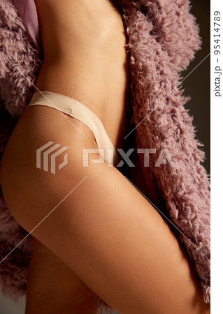Cropped image of smooth, tanned female body, hip, legs. Woman posing in underwear and pink furry coat. No cellulite 95414789