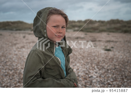 Portrait of freckles handsome blond boy on beach on windy day. Alone child with hood walking on sandy beach. Autumn. Portrait of freckles handsome blond boy on beach on windy day. Alone child with hood walking on sandy beach. Autumn. 95415887