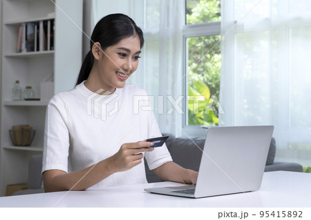Asian woman holding credit card and using laptop computer 95415892