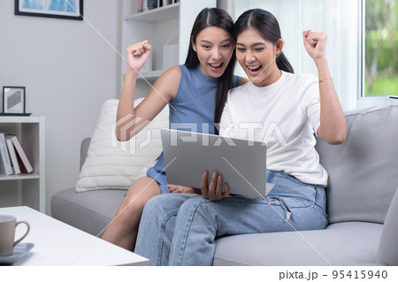 Asian lesbian couple  using laptop in the living room. happily raising their hands up 95415940