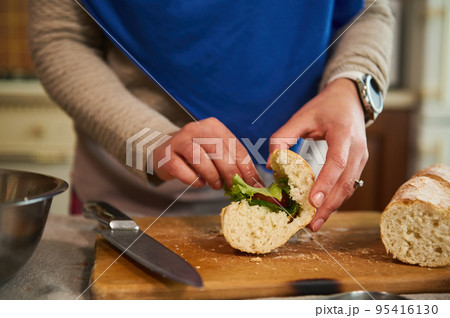 Details: Woman's hands put greens and organic fresh vegetables in the bread, making crusty sandwiches with veggies in the home kitchen, preparing a delicious healthy snack Details: Woman's hands put greens and organic fresh vegetables in the bread, making crusty sandwiches with veggies in the home kitchen, preparing a delicious healthy snack 95416130
