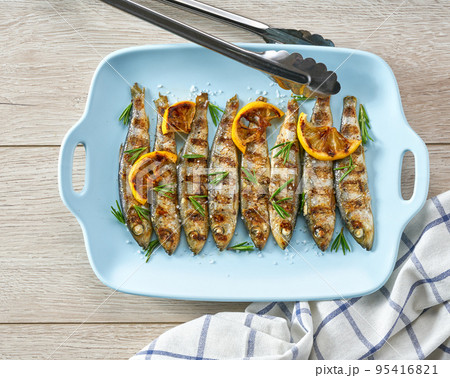 Grilled sardines with salt, herbs and lemon slices on a white table, top view. Grilled sardines with salt, herbs and lemon slices on a white table, top view. 95416821