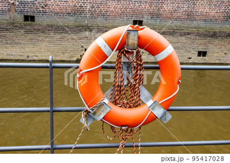 Orange lifebuoy on a berth fence by a river Orange lifebuoy on a berth fence by a river 95417028