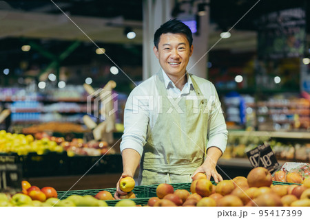 Portrait of Asian supermarket salesman, man in grocery vegetable section smiling and looking at camera. 95417399