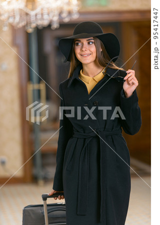 Happy young woman in hat with travel bag walking inside hotel 95417447