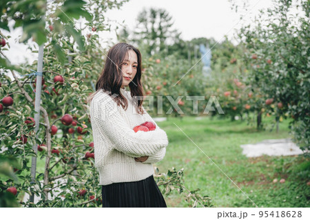 赤いりんごを持った白いニットを着た女性のポートレート 95418628